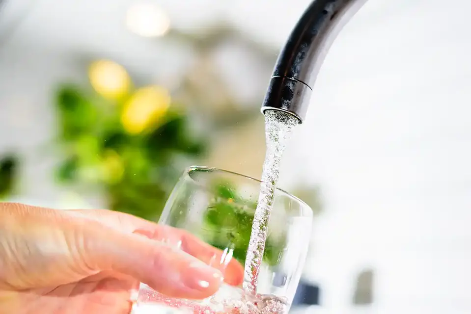 Vattenkran med hand som håller glas